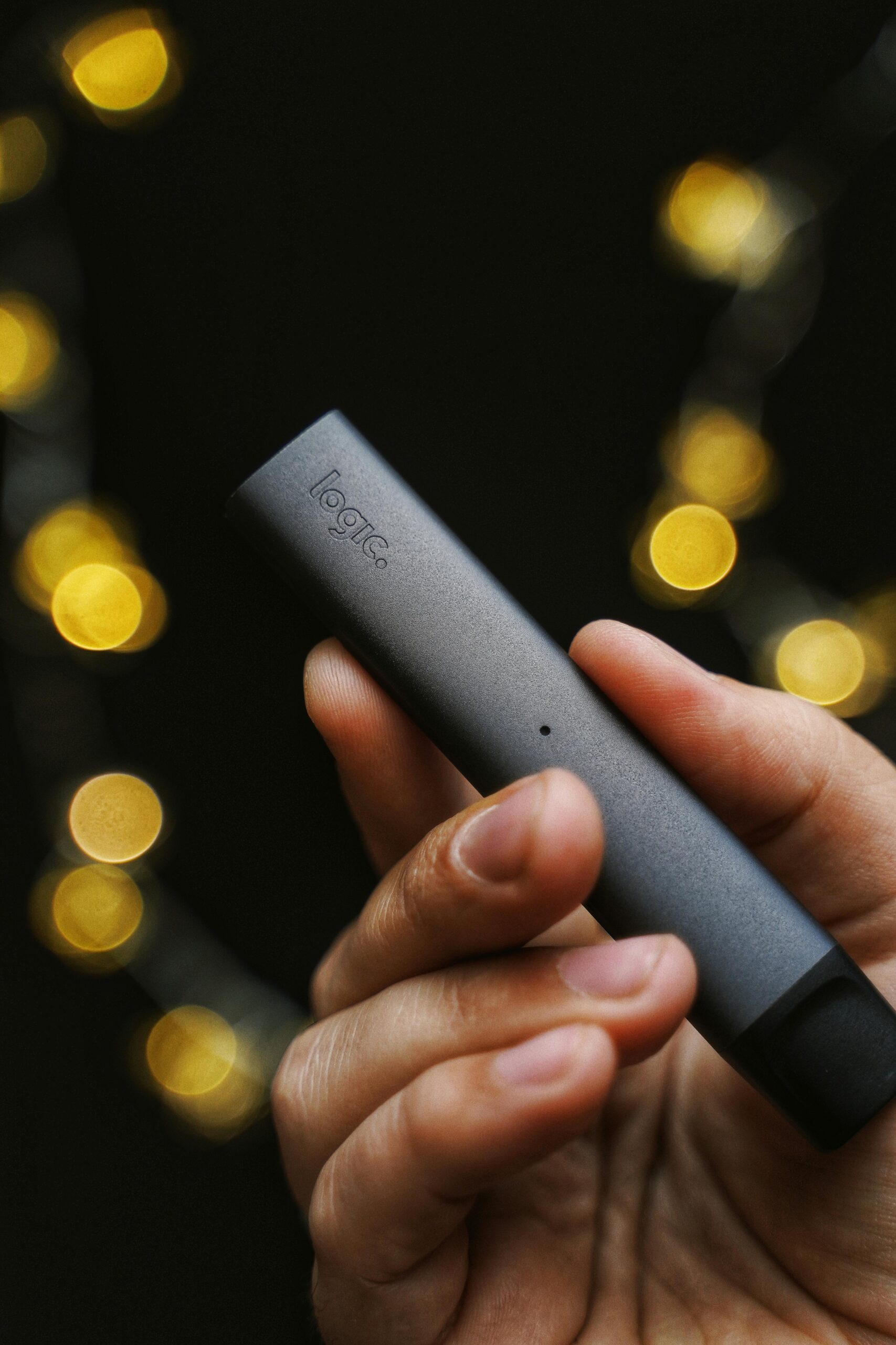 Detailed shot of a hand holding a sleek e-cigarette with bokeh lights in the background.